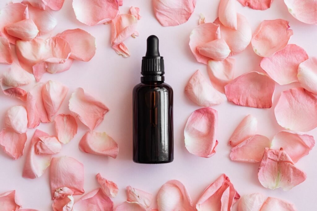 From above composition of soft petals of roses placed around brown vial with dropper on pink surface